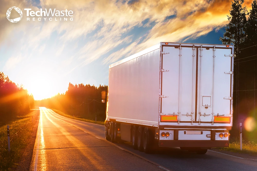 TWR- A large white semi-truck drives down a rural highway at sunset with "TechWaste Recycling" logo in the top left corner, highlighting ITAD best practices for secure and responsible electronics disposal.