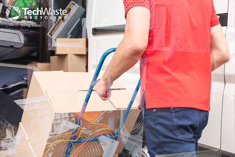 A person in a red shirt loads a box of electronic waste onto a cart near a van, with the TechWaste Recycling logo in the corner.