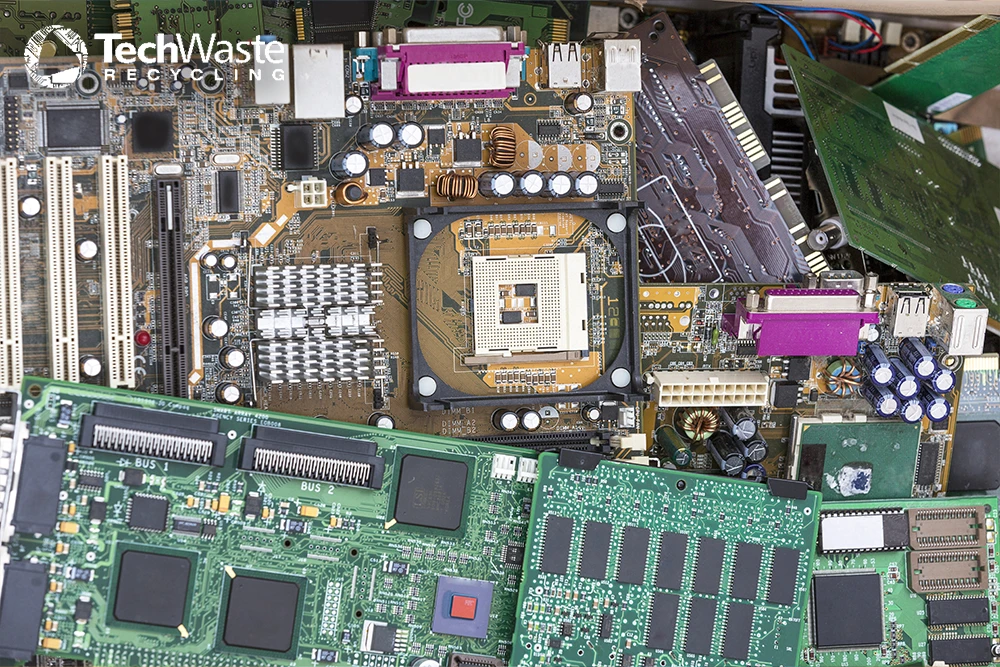 A pile of various discarded computer circuit boards with electronic components, showing connectors, chips, and memory modules.
