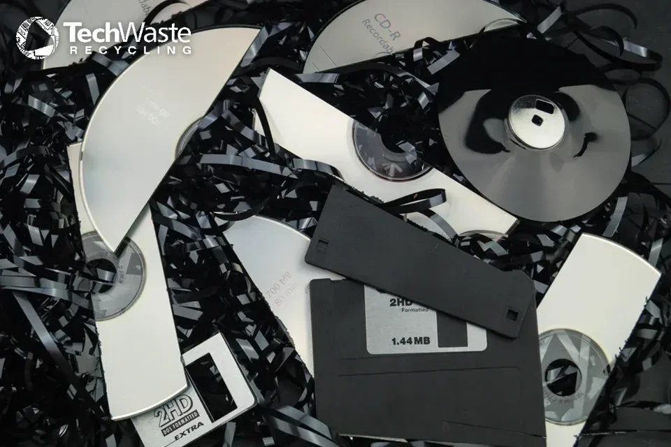 Shredded magnetic tape, broken floppy disks, and CDs are shown, illustrating electronic media ready for recycling. The TechWaste Recycling logo appears in the top left corner.