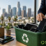 Person places used smartphones into a green recycling bin, with a city skyline in the background and TechWaste Recycling logo visible.