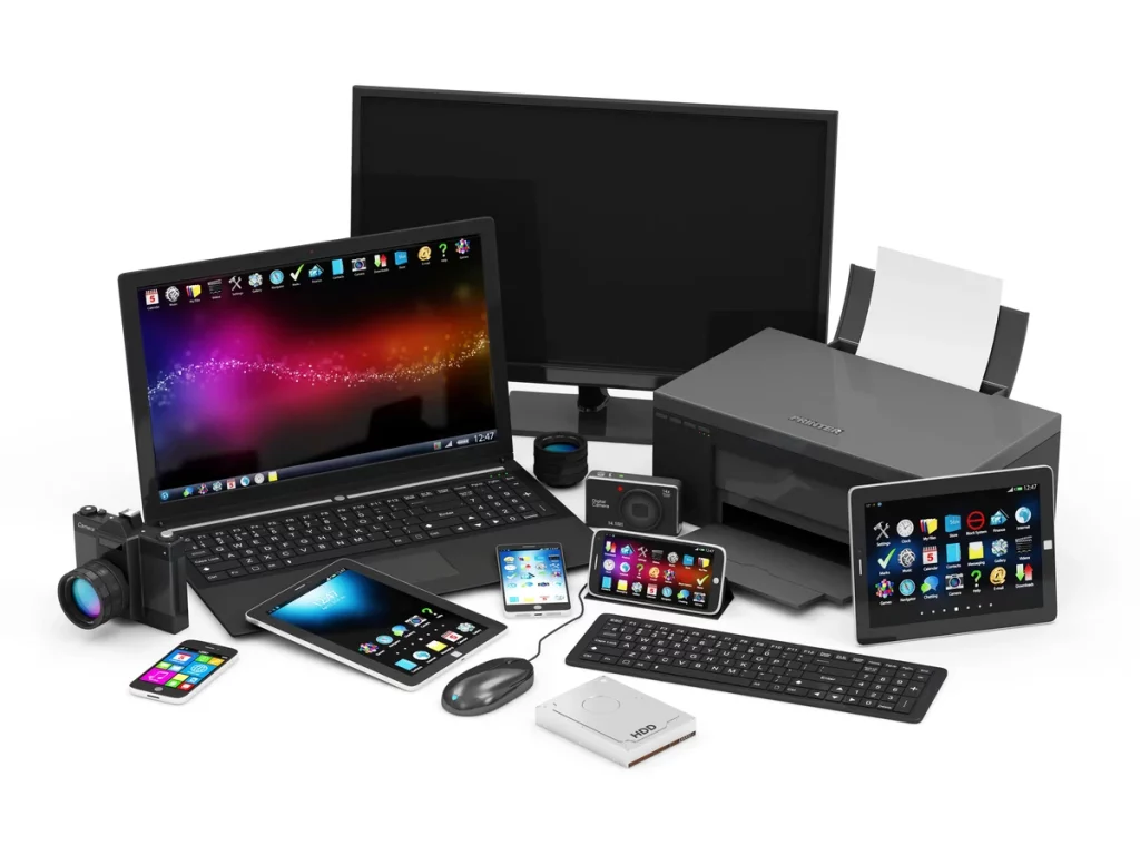 Assorted electronic devices including a laptop, monitor, printer, tablet, smartphone, camera, keyboard, mouse, and other gadgets arranged together on a white surface.