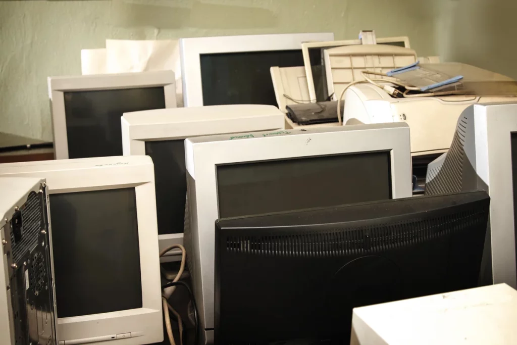 A collection of old computer monitors, keyboards, and electronic devices stacked closely together in a room.