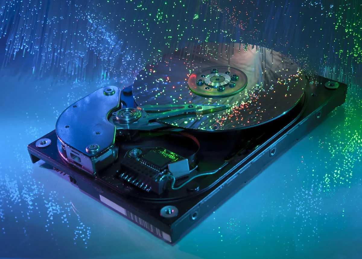 A close-up of an opened hard disk drive with colorful fiber optic lights reflecting off its shiny platter, creating a technological aesthetic.