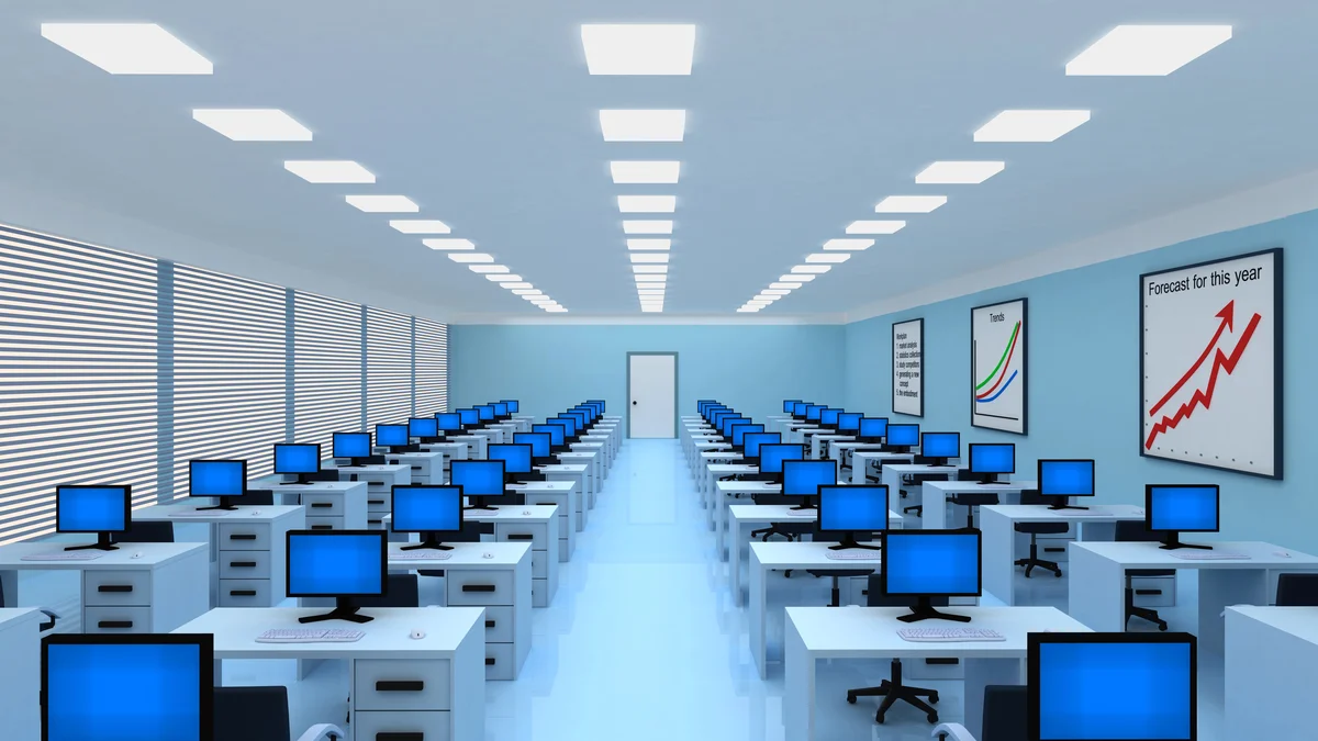 Rows of desks with computers in a brightly lit office. Several charts with upward trends are displayed on the walls. The room appears empty of people.