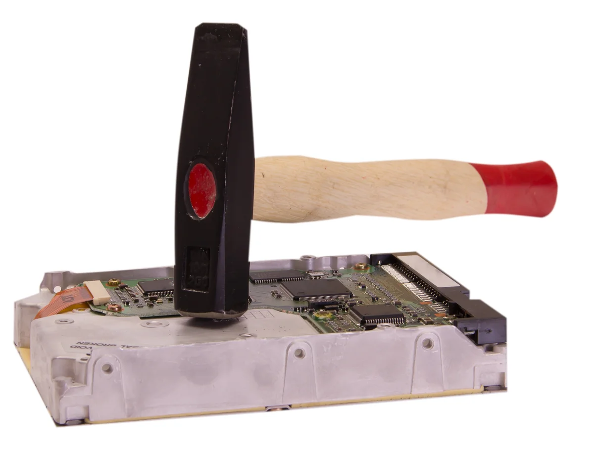 A hammer rests on top of a computer hard drive, suggesting potential damage or destruction of the device.