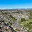 Aerial view of a suburban neighborhood with rows of houses, streets, and a green park area under a clear blue sky.