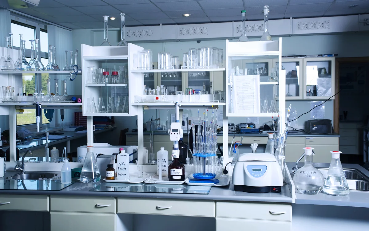 A clean, modern laboratory with glassware, scientific equipment, and chemicals neatly arranged on counters and shelves.